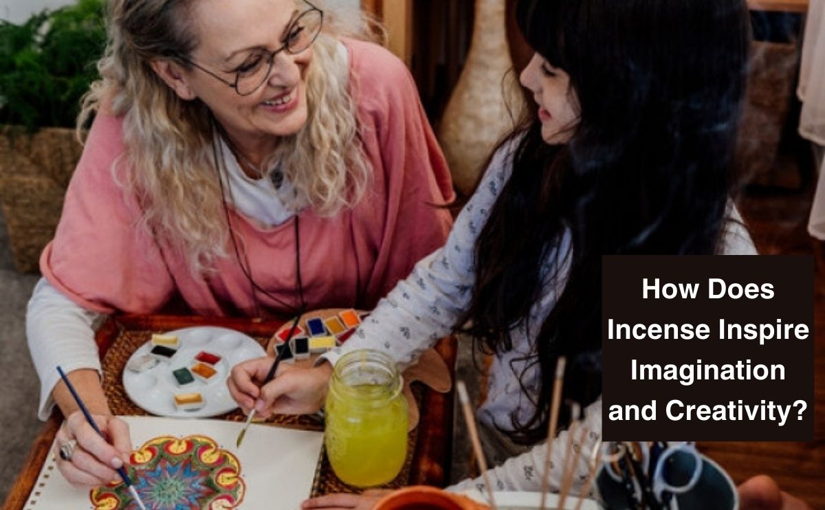 Two women painting a colorful mandala with watercolors, incense sticks on table nearby.