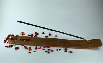 Rose incense stick on wooden holder with scattered rose petals on white background