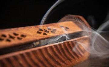 Burning incense stick in carved wooden holder with smoke rising, dark background