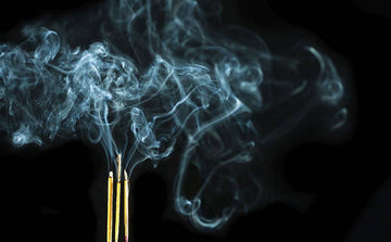 Burning incense sticks with fragrant smoke swirling against a dark background